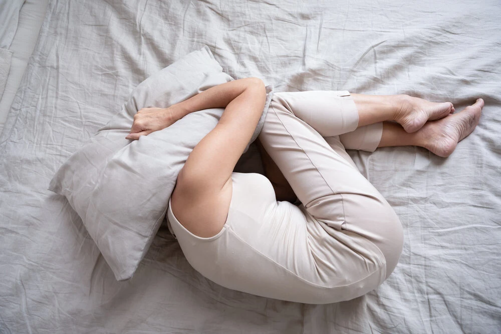middle aged woman lying alone on bed in fetal position covering head with pillow feeling afraid or depressed suffer from insomnia