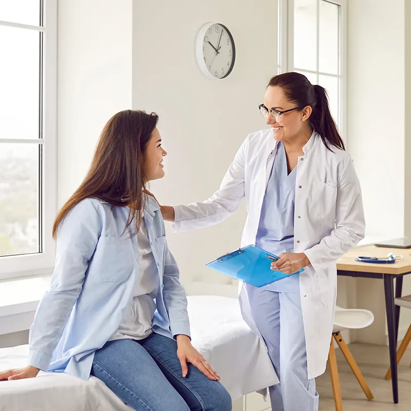 Happy young pregnant woman talking with her gynecologist doctor in hospital or medical clinic.
