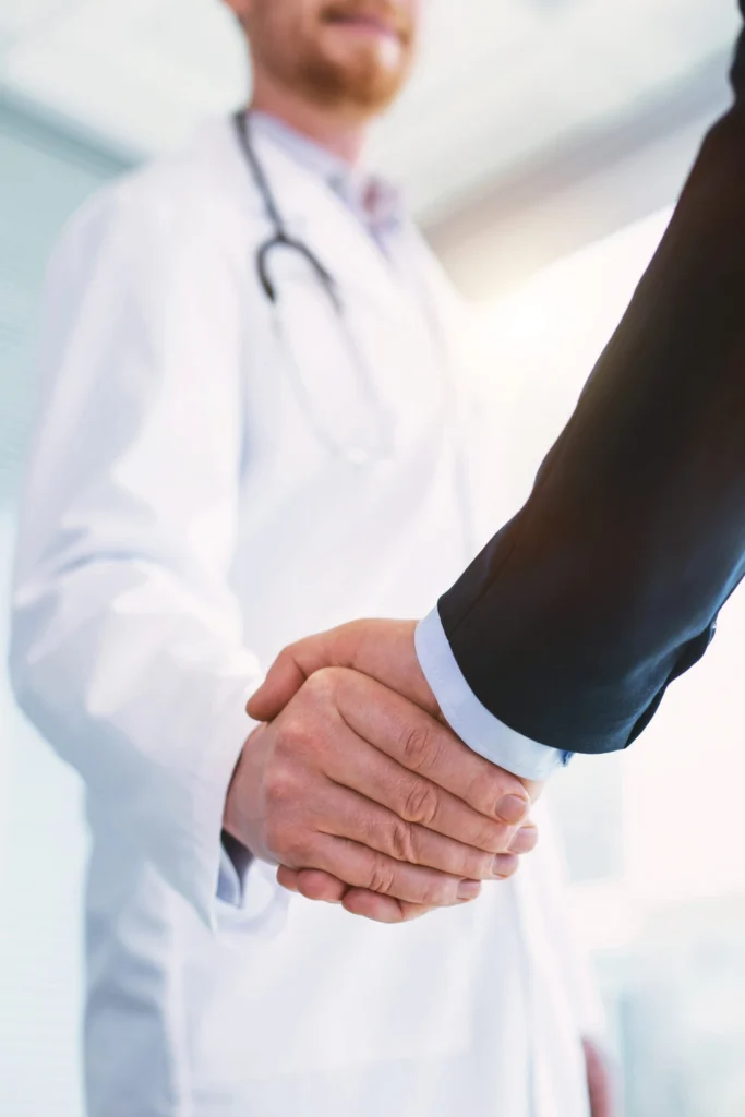 Inspired professional doctor wearing a uniform and shaking hands with a businessman